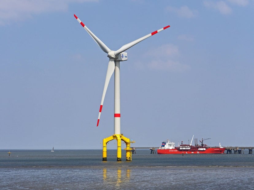 an offshore wind farm propeller in the foreground with and LNG carrier moored behind it