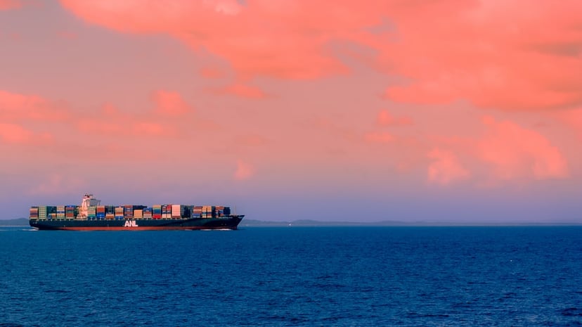 container ship sailing under pink sky