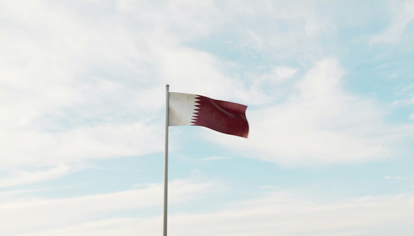 The flag of Qatar flying against a blue and white cloudy sky