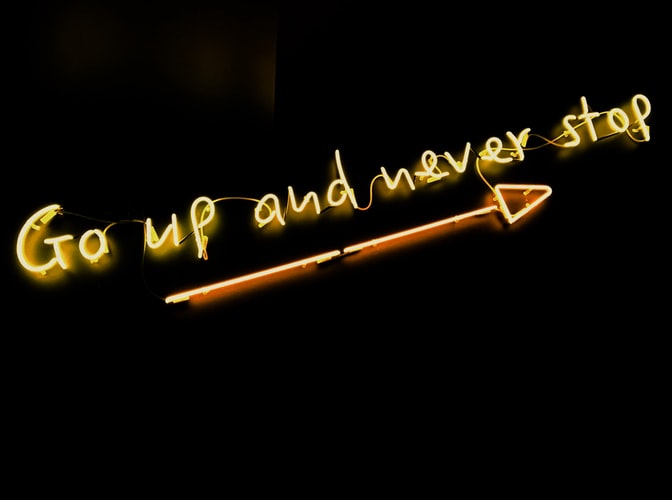A gold neon sign with an arrow and the words 'go up and never stop'
