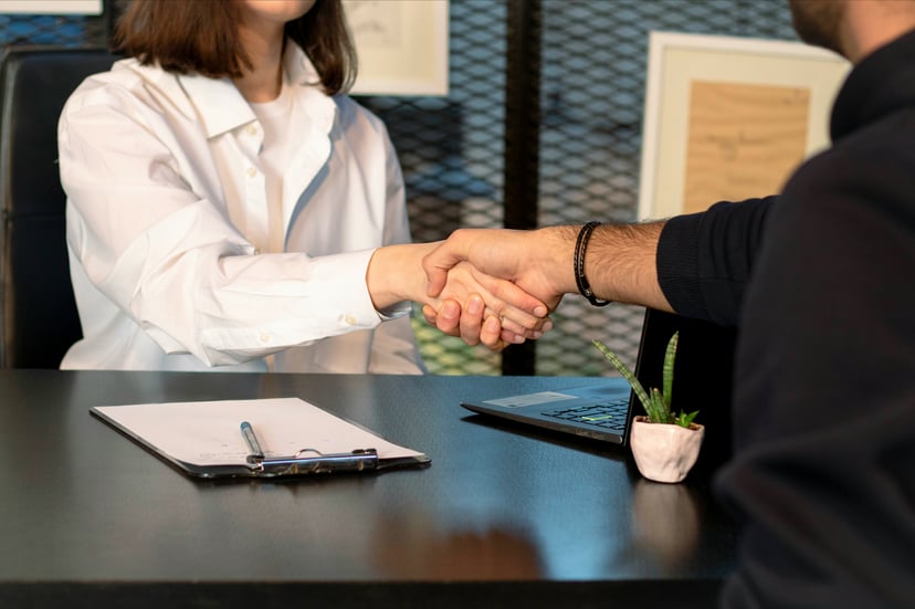 a man and woman shaking hands across a desk in a job interview