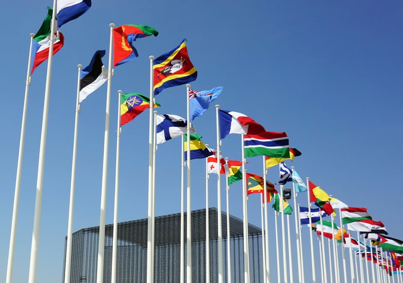 Different countries' flags flying on flagpoles against a blue sky