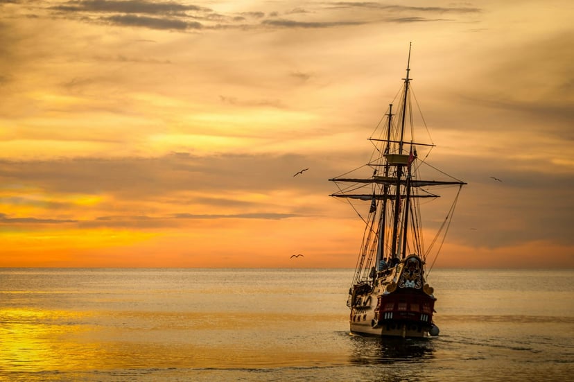 a sailing ship at sea as the sun sets