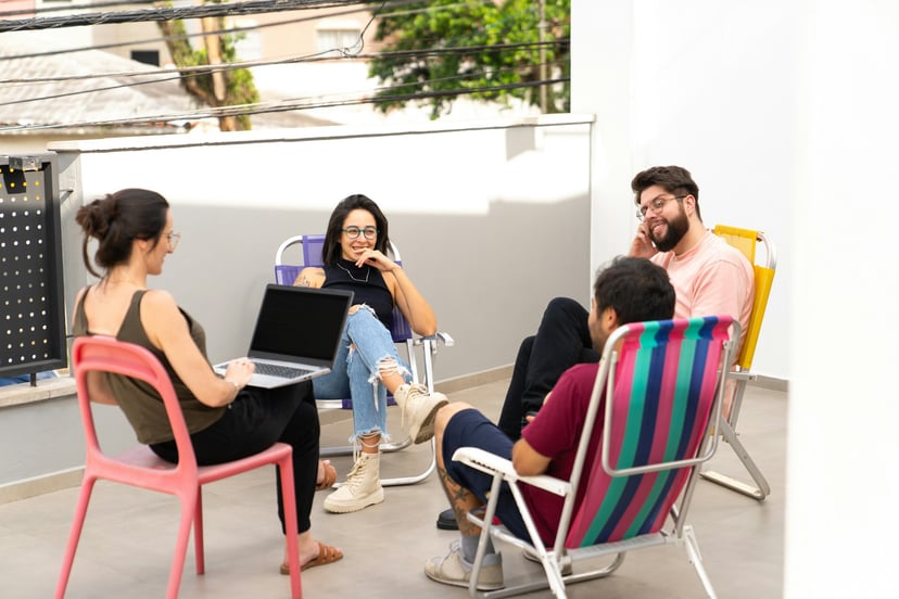 Group of young people sitting in deckchairs, chatting and using a laptop