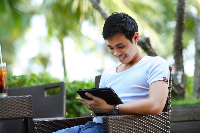 a smiling man sitting outside and using a tablet PC