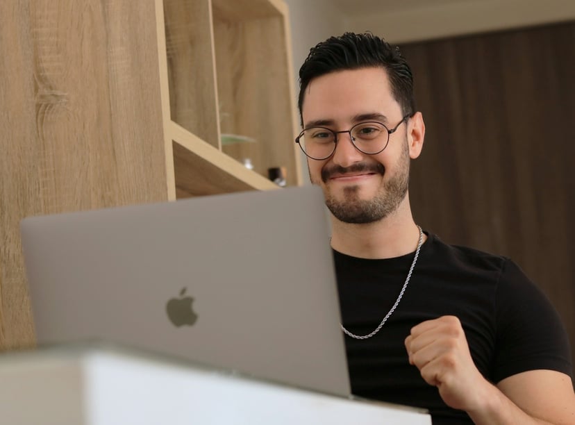 a please looking man using his laptop and clutching his fist in an expression of joy