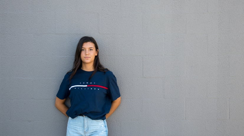a young woman leaning against a wall and wearing a navy Tommy Hilfiger logo t-shirt