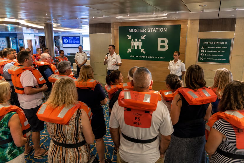 passengers on a cruise ship wearing life jackets and attending a muster drill