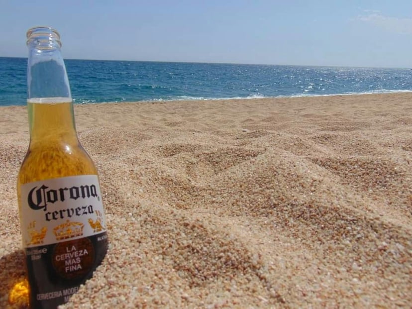 a bottle of Corona beer wedged into sand on a beach