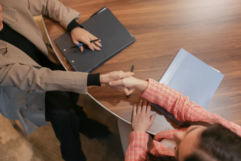 two people shaking hands across a desk in a job interview