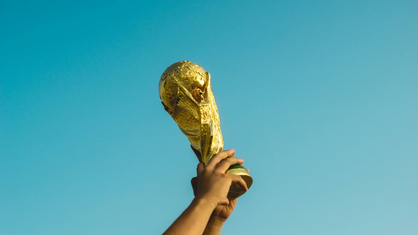 A hand holding the World Cup trophy up against a blue sky