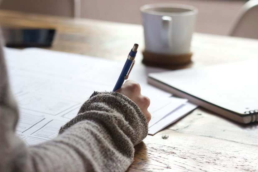 A person writing on paper with a cup of coffee nearby