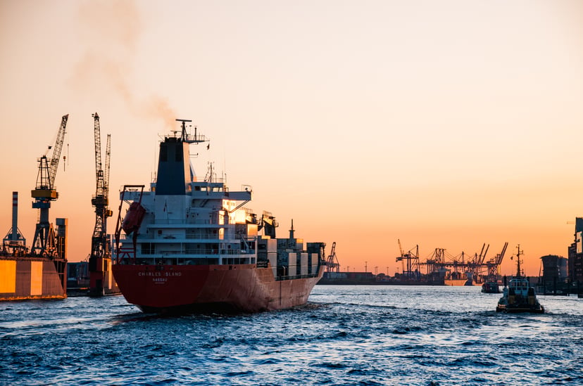a cargo ship with the superstructure clearly shown, sailing through a port at sundown