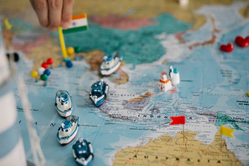 a hand placing an Indian flag on a map of India next to toy boats