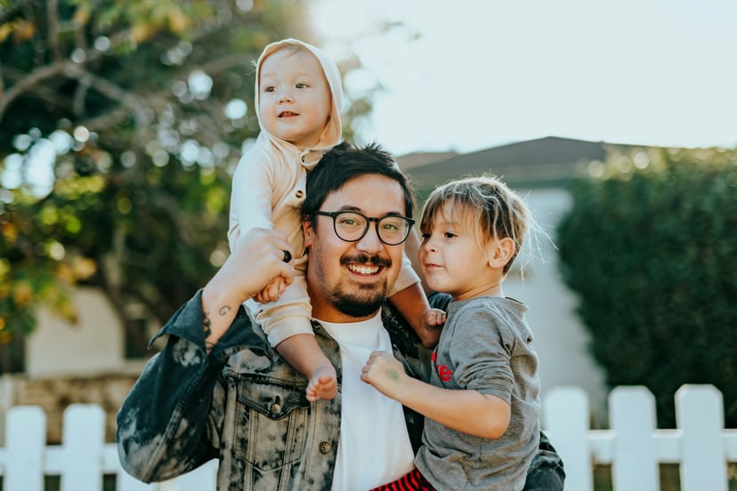 A smiling dad holding his two young kids