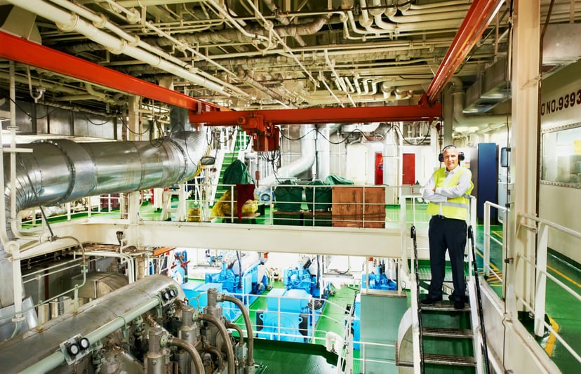 A marine engineer standing on a staircase in a ship's engine room