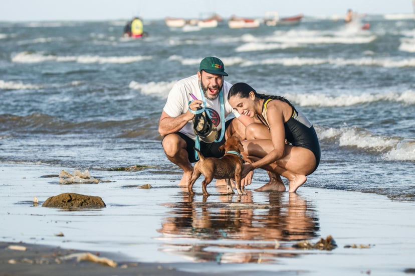 a couple on their dog on a beach looking pleased at something they've found