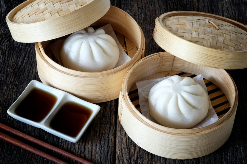 Baozi in a bamboo steamer with a dish of soy sauce