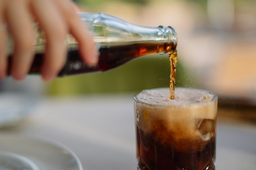 A hand pouring a bottle of soda into a glass