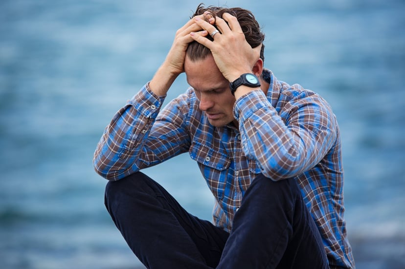 Man sitting by water with his head in his hands