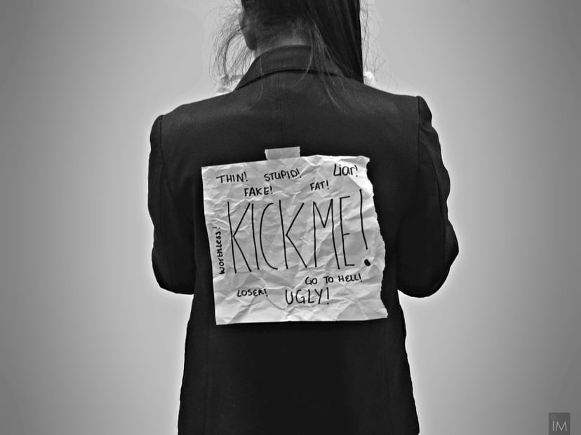 Person with a bullying sign on their back saying 'kick me'
