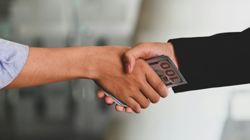 Two people shaking hands while one passes money to the other in the palm of his hand