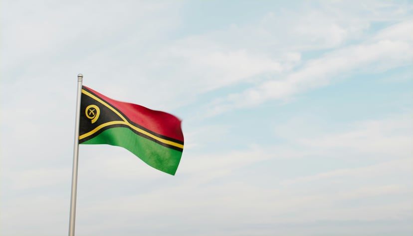 The flag of Vanuatu flying against a blue and white sky