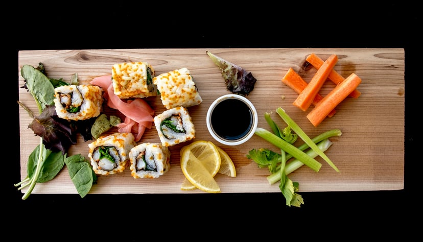 a wooden platter of sushi and garnish such as carrots
