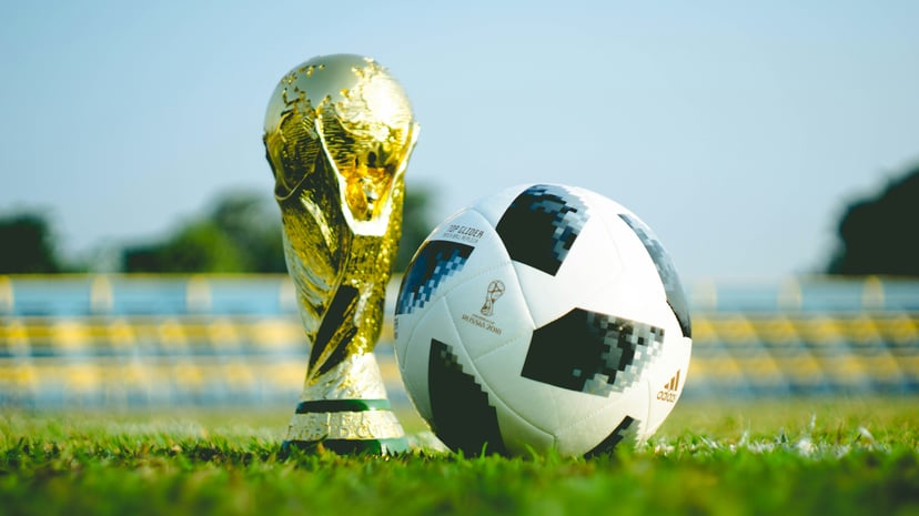 A football and the FIFA World Cup trophy on a football pitch