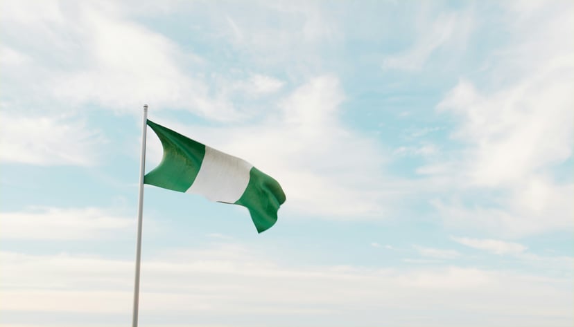 The Nigerian flag flying in front of a blue cloudy sky