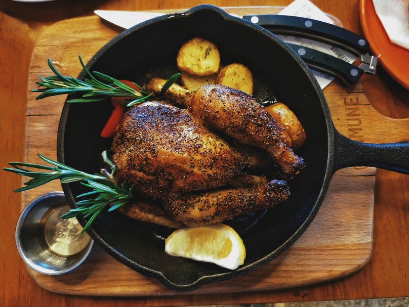 Roast chicken in a frying pan with potatoes and fresh herbs
