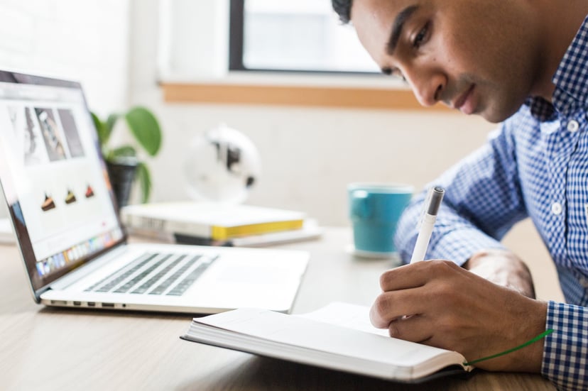 a man sitting at a laptop writing in a notebook