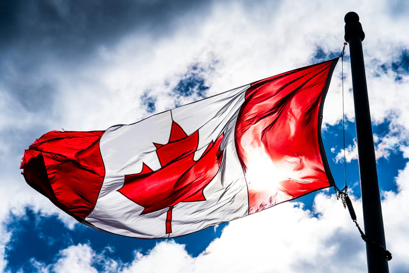 The Canadian flag flying in front of a blue cloudy sky