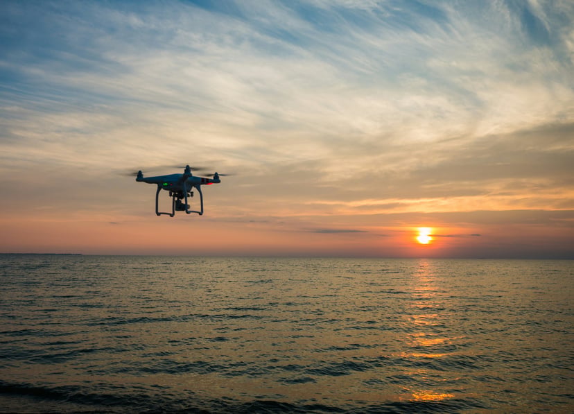 a drone flying over a body of water at the sun sets on the horizon