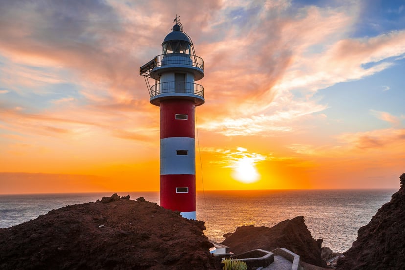 A red and white striped lighthouse with the sun setting in the background