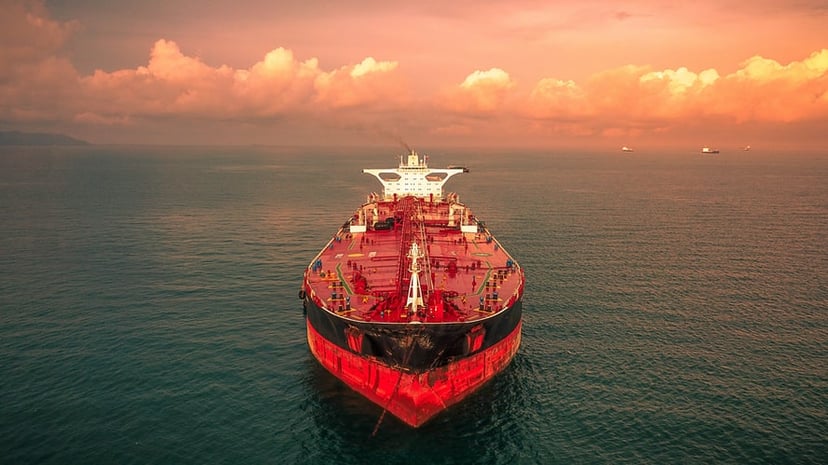 a red and black oil tanker on the ocean at sunset