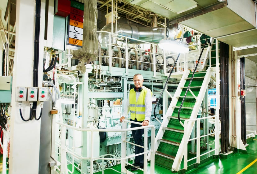 A marine engineer standing on a staircase in a ship's engine room