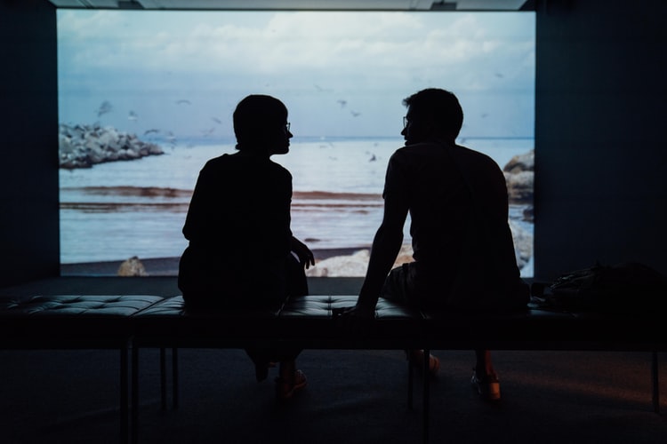 Silhouette of two people sitting in front of the ocean talking