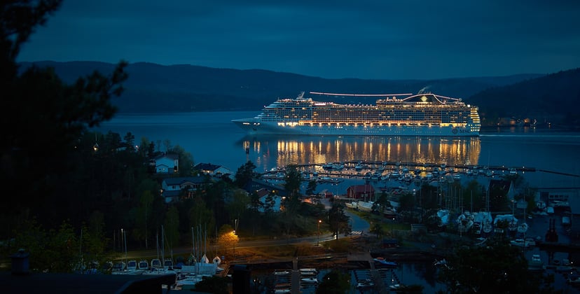 The MSC Preziosa cruise ship lit up at night and sailing near a shoreline