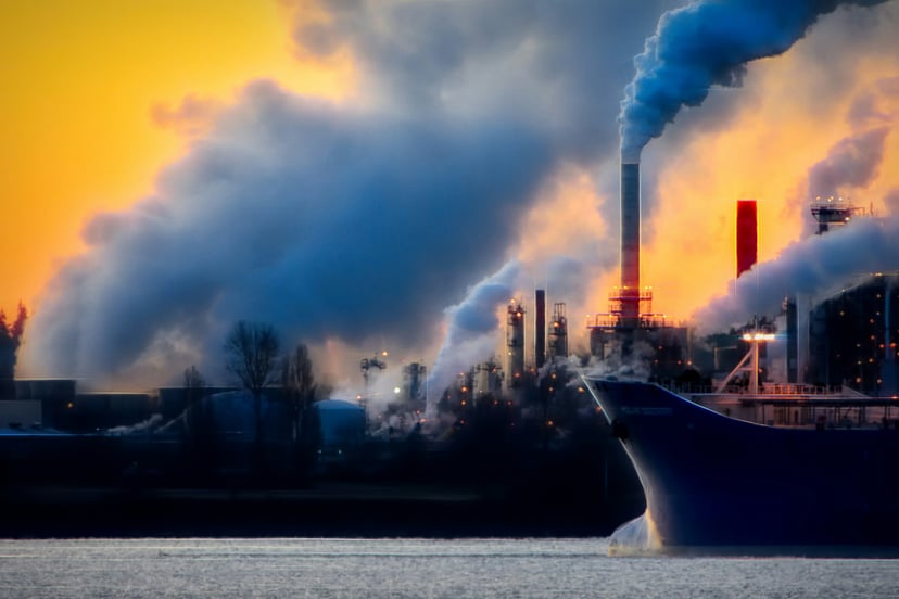a cargo ship sailing past factories pumping out emissions into the air