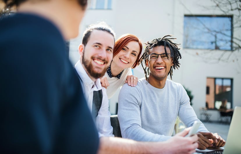 three smiling people using a laptop 