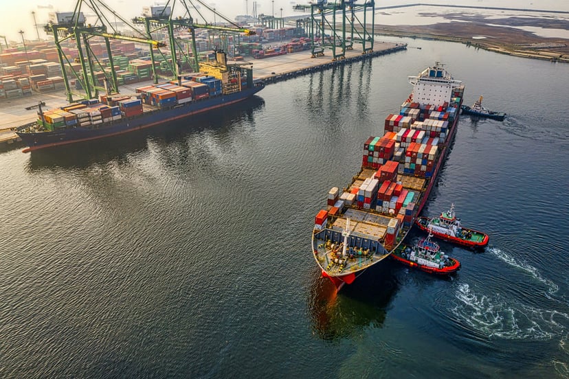 an aerial view of a container ship and tugboats in port
