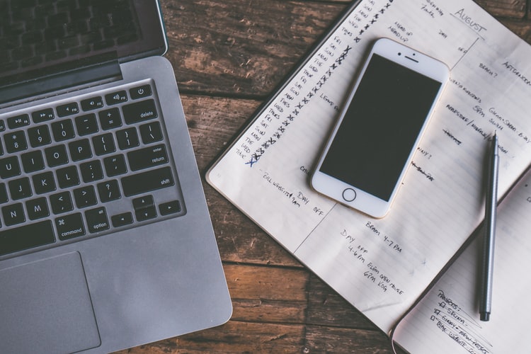 A laptop, iPhone and checklist in a notepad on a desk
