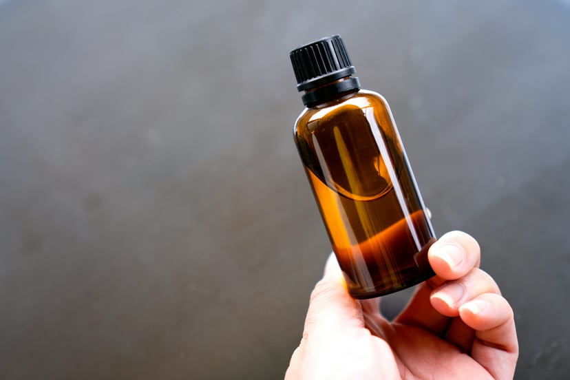 A hand holding a small brown bottle of liquid