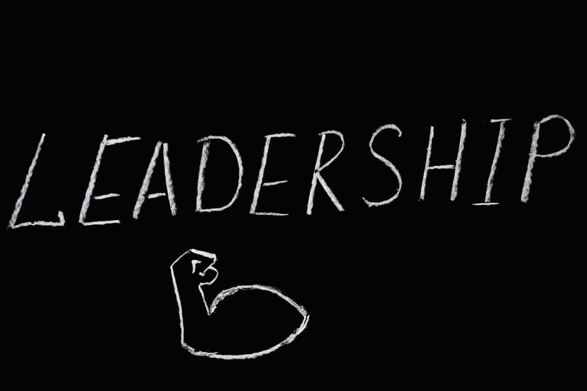 The word 'leadership' written on a chalkboard with a drawing of a bulging bicep underneath