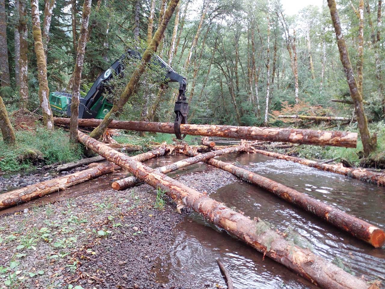 Large pieces of wood are placed in the streambed of Rock Creek in Clatsop State Forest to improve habitat for fish and other wildlife. The project was completed in conjunction with a contract timber sale to reduce costs. The excavator, run by an operator from Bighorn Logging, placed 30 trees into the stream at five locations.