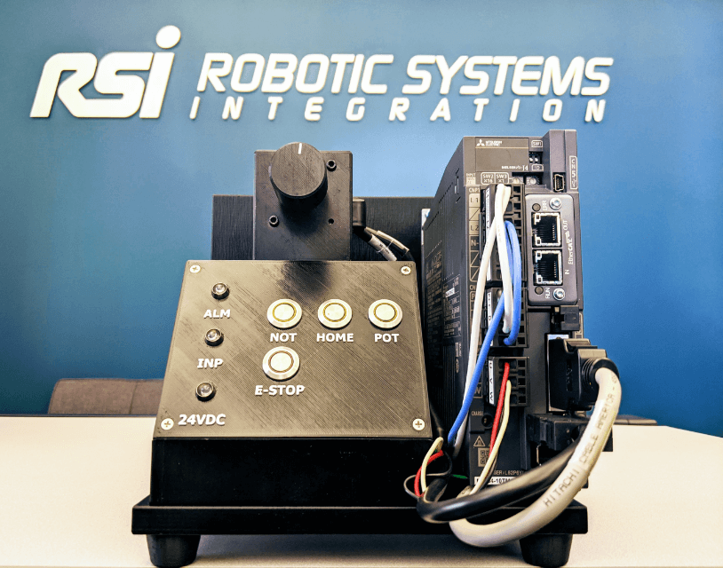 Demo unit with a pushbutton control panel and wired servo drive in front of an RSI logo backdrop