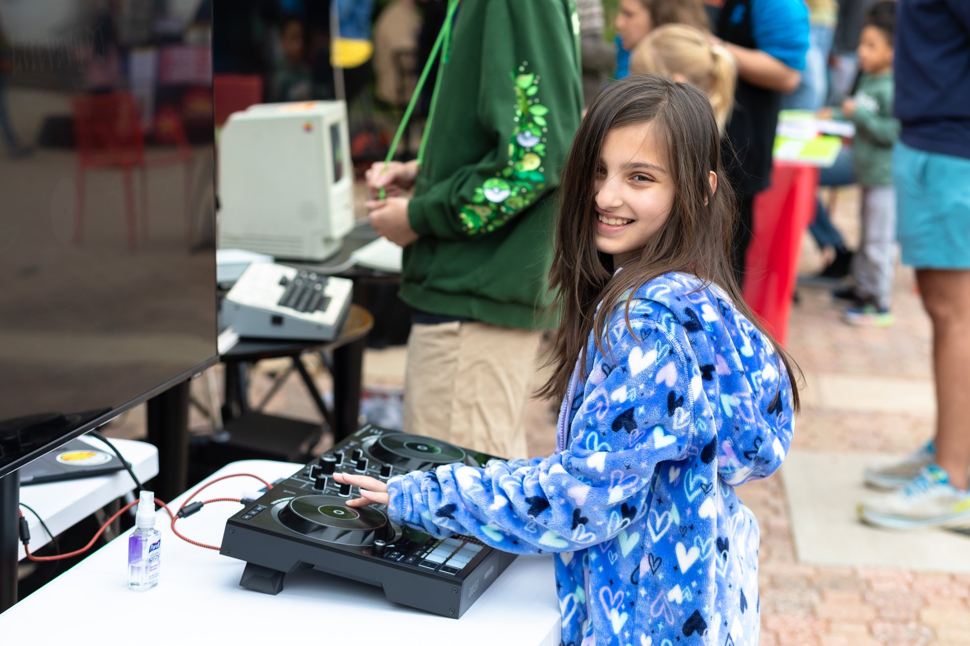 A smiling child at the DJ controller at an outdoor LiteraryDJ table.