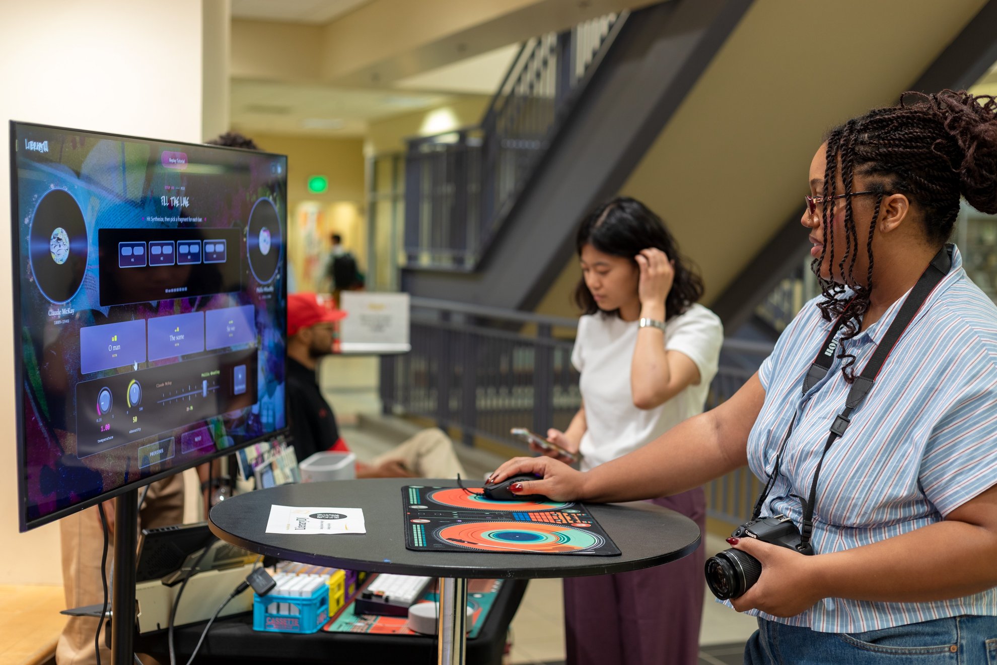 Two visitors at a LiteraryDJ table in a library lobby, one with a camera.