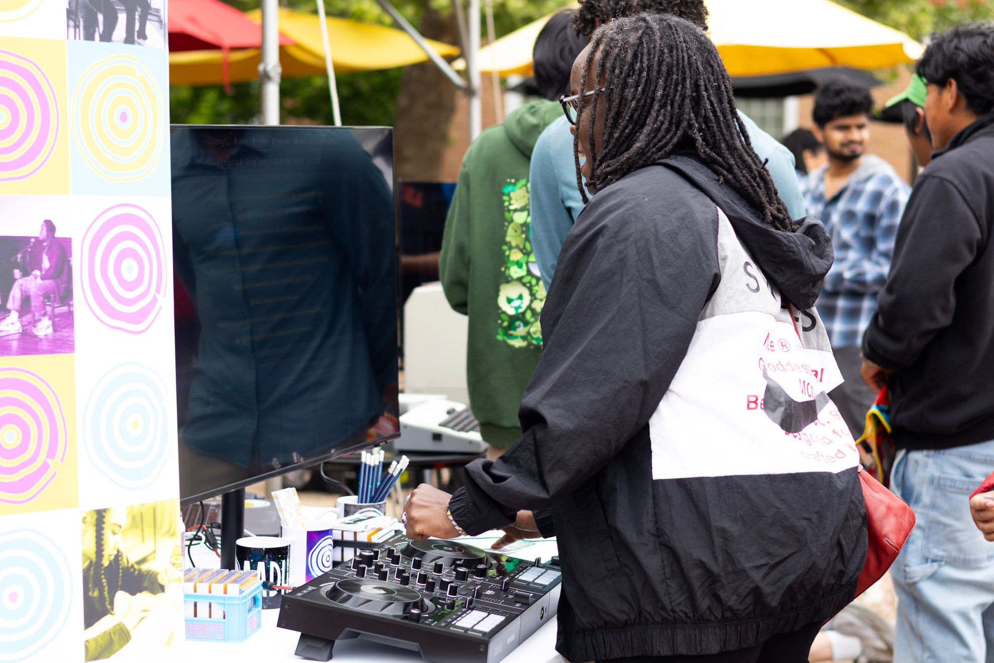 A visitor at the DJ controller at an outdoor LiteraryDJ table, with a crowd behind.